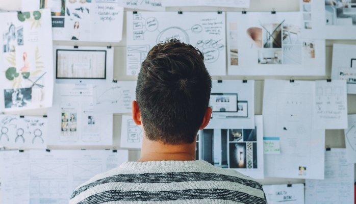 Man looking at a board filled with work related pictures and diagrams.